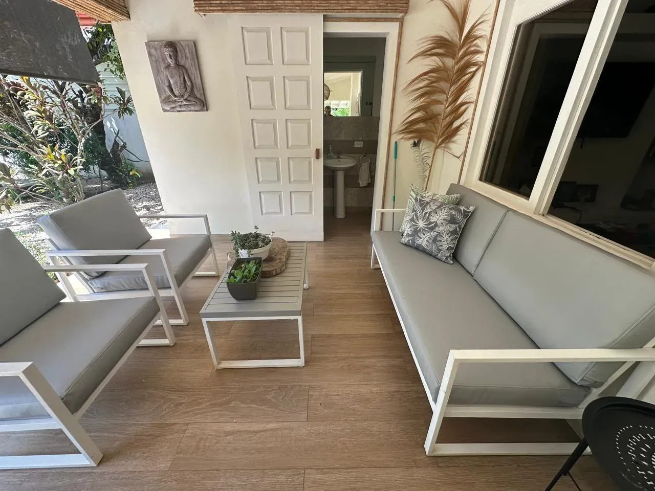 Outdoor lounge with white modular sofa and armchairs with beige cushions on a wood-look floor.
