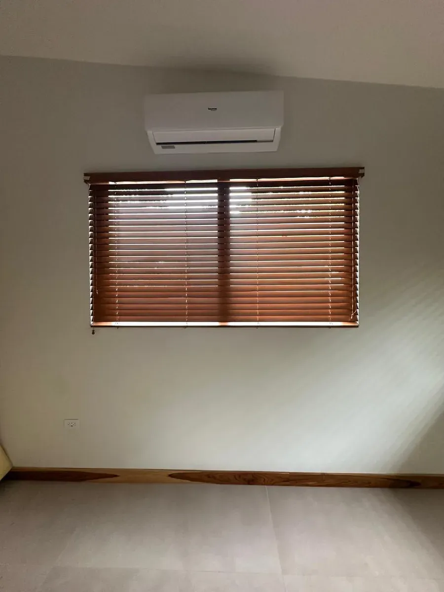 Horizontal mahogany-toned wood blinds across a window with a split air-conditioner above.