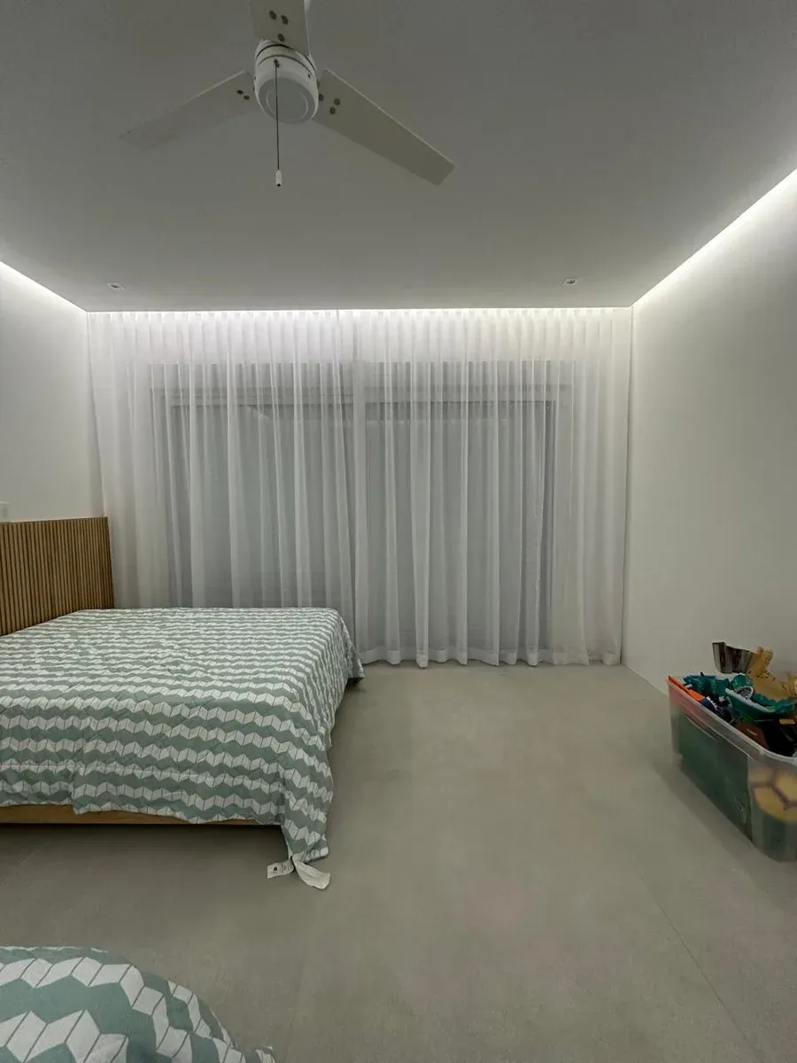 Bedroom with floor-to-ceiling white sheer drapes, ceiling fan, and wood-paneled headboard wall.