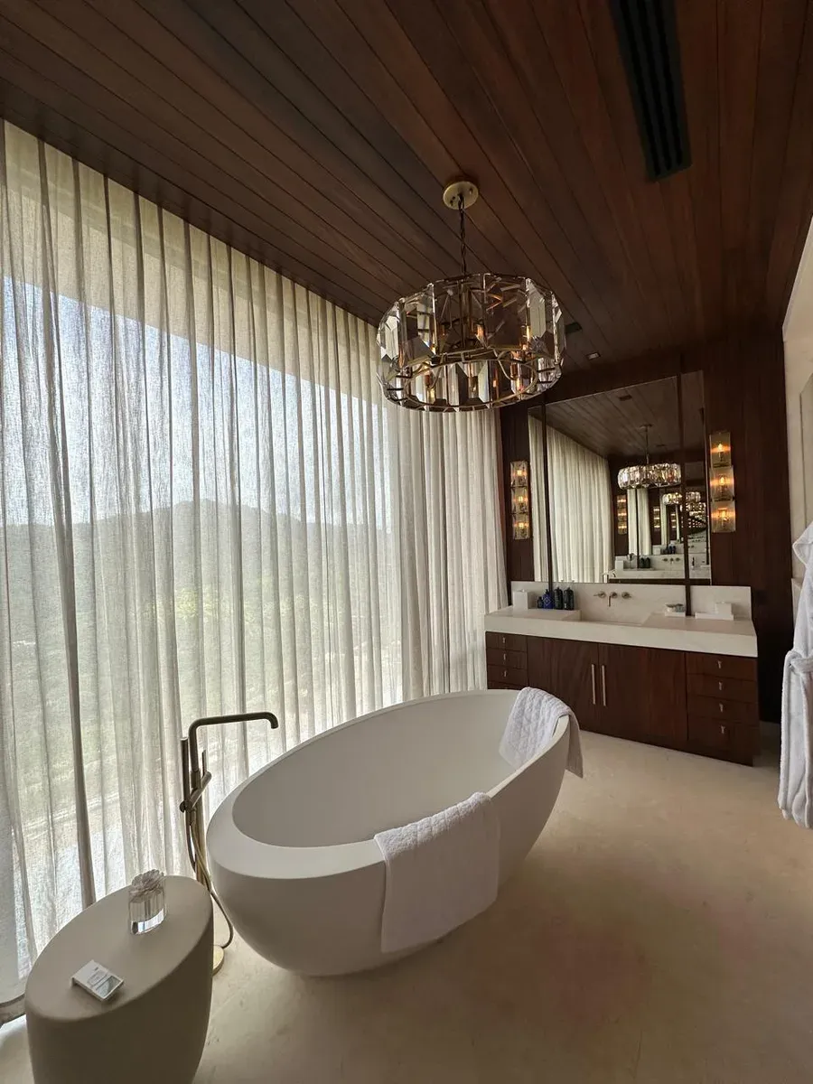 Bath with full-wall floor-length sheer drapes, oval soaking tub, and faceted crystal chandelier.