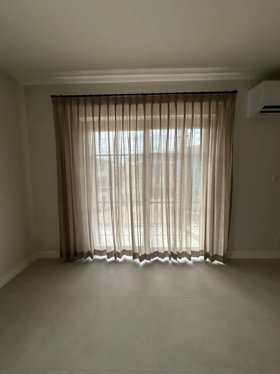 Sand-toned pleated drapes framing a wide window with a split air-conditioner on the right.