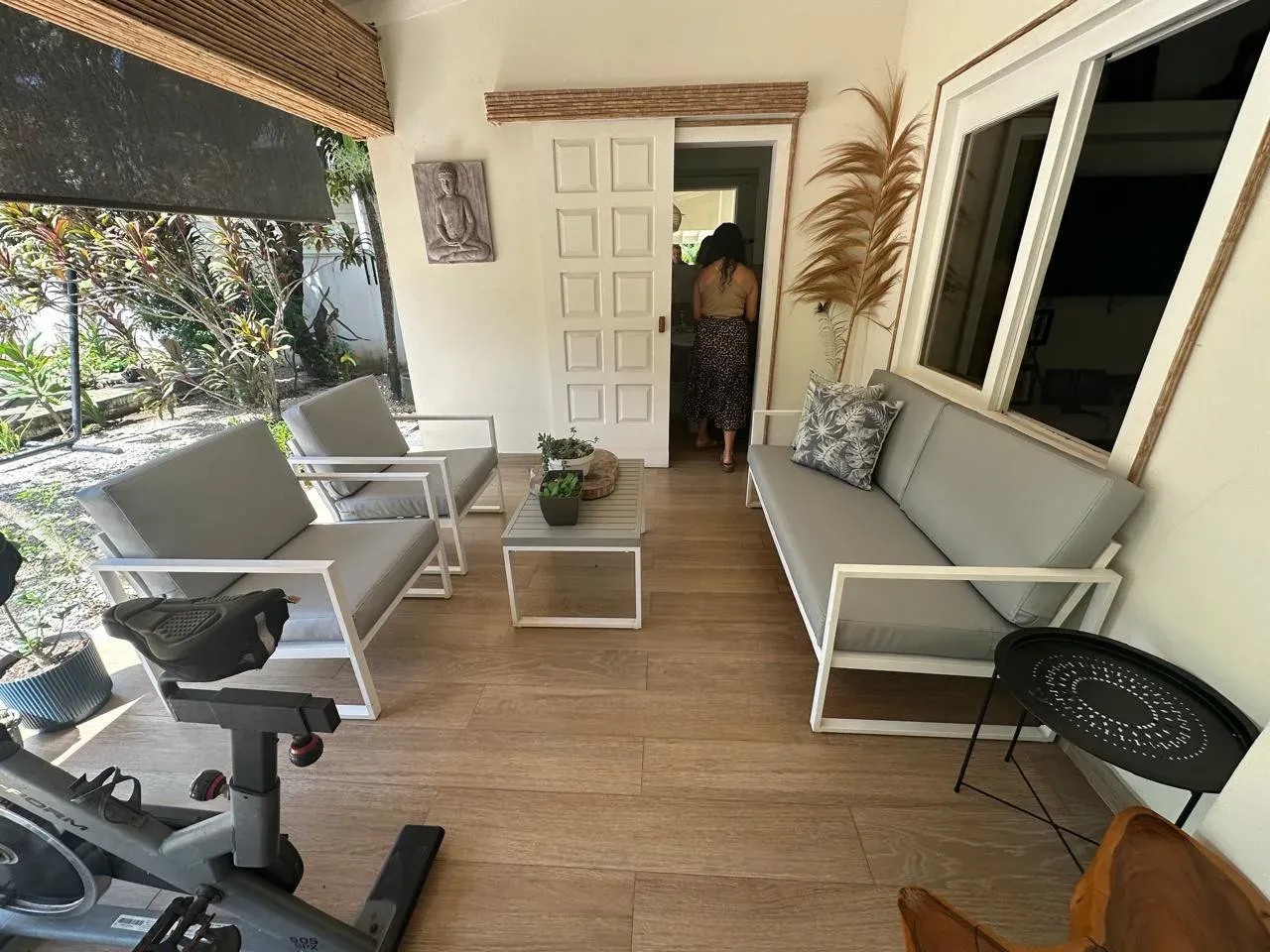 Covered terrace with white modular sofa and armchairs with beige cushions on a wood-look floor.