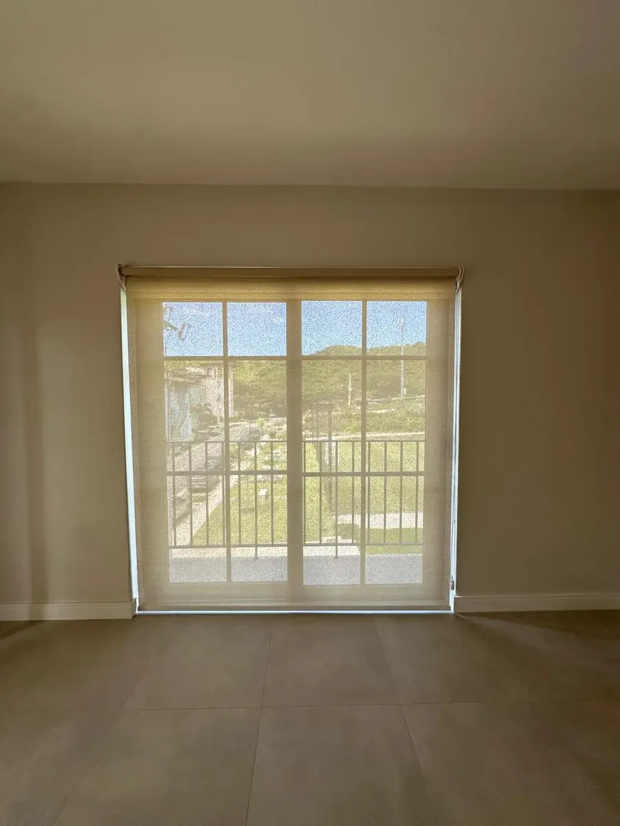 Sand-toned screen roller shade over a sliding glass door with a dry-landscape view.