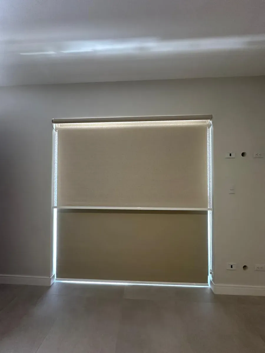 Two ivory blackout roller shades half-lowered with light filtering in from the sides.