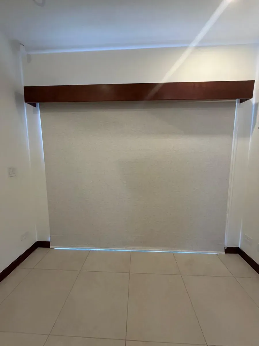 Cream screen roller shade beneath a dark-wood pelmet against a white wall.