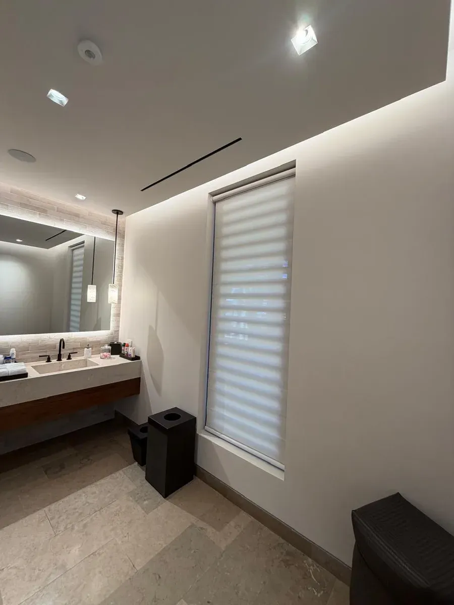 Modern bath with white day-and-night shade, concrete sink, and back-lit illuminated mirror.