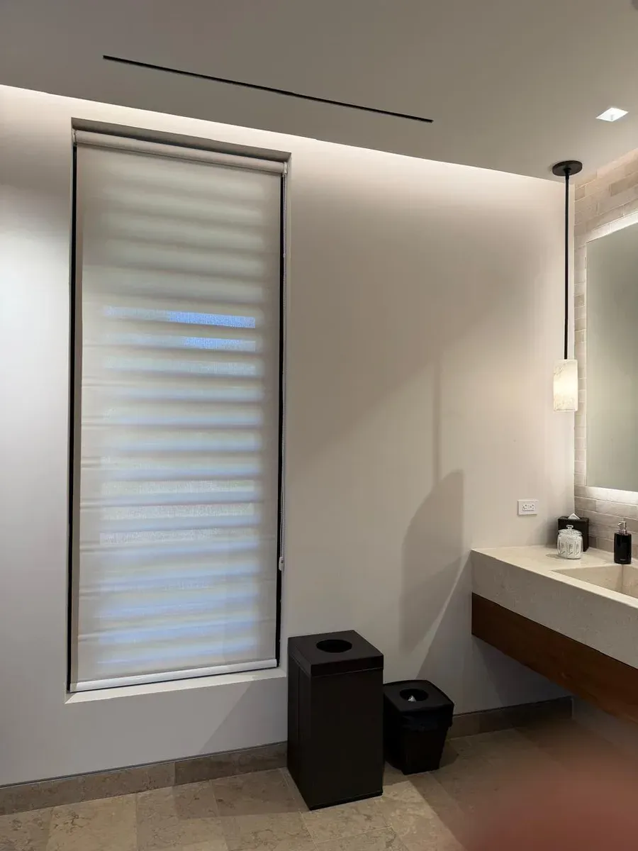 White day-and-night shade half-raised beside a concrete sink in a bath with a back-lit mirror.