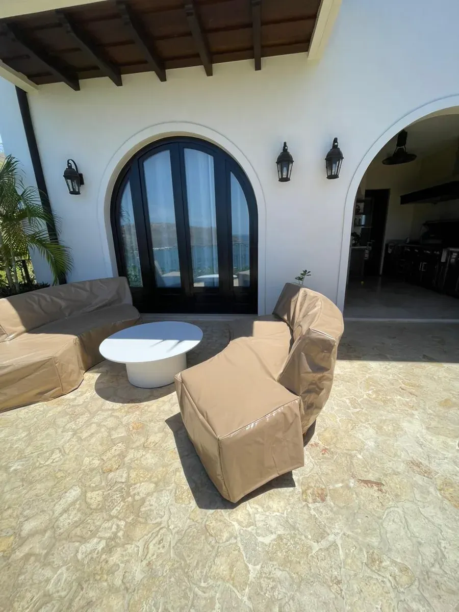 Colonial patio with covered furniture, round white table, and arched French door with sea view.