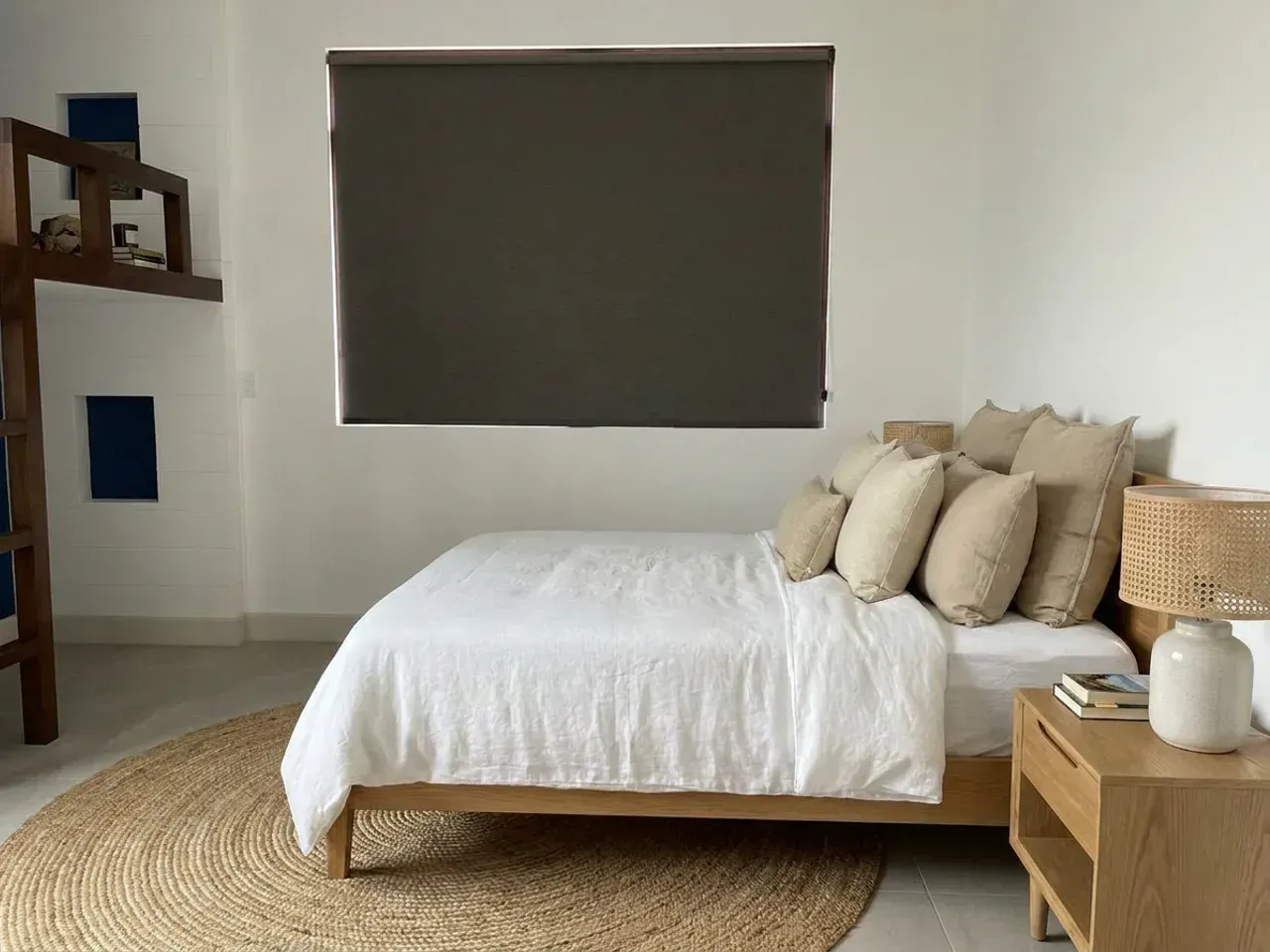 Dormitorio con Roller Blackout gris oscuro bajado por completo sobre la ventana, cama vestida en lino y alfombra de yute.